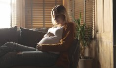 Lächelnde Schwangere sitzt auf Sofa und berührt ihren Bauch — Stockfoto