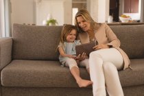 Mère et fille utilisant une tablette numérique dans le salon à la maison — Photo de stock