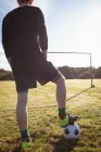 Sección baja del jugador de fútbol de pie con pelota de fútbol en el campo - foto de stock