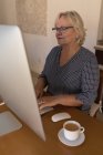 Старшая женщина, работающая дома за компьютером — стоковое фото