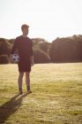 Jogador de futebol de pé com bola de futebol no campo em um dia ensolarado — Fotografia de Stock