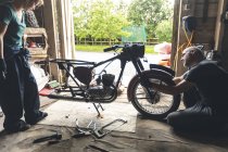 Механики мужского и женского пола ремонтируют мотоцикл в ремонтном гараже — стоковое фото