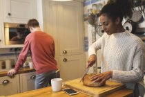 Donna che taglia pane in cucina a casa — Foto stock