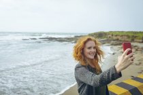 Donna rossa che si fa selfie con il cellulare in spiaggia . — Foto stock