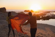 Paar vergnügt sich mit Decke am Strand bei Sonnenuntergang — Stockfoto