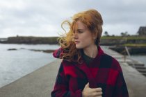 Thoughtful redhead woman standing in the beach in wind. — Stock Photo