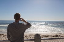 Vista trasera del hombre hablando por teléfono móvil cerca de la playa - foto de stock