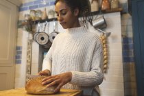 Жінка ріже хліб на кухні вдома — стокове фото