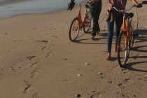 Baixa seção de casal com bicicletas andando na praia — Fotografia de Stock