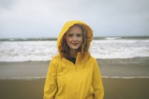 Portrait of redhead woman in yellow jacket standing in the beach. — Stock Photo