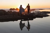 Rear view of couple holding hands while standing on beach during sunset — Stock Photo