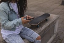 Mid section of female skateboarder using mobile phone in city — Stock Photo