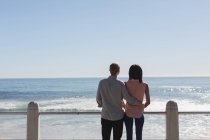Rear view of couple standing together near railing at beach — Stock Photo