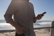 Sección media del hombre utilizando el teléfono móvil cerca de la playa - foto de stock