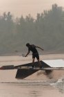 Joven atleta wakeboarding en el río al atardecer - foto de stock