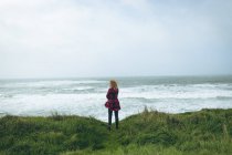 Вид сзади на рыжую женщину, стоящую на травянистом пляже . — стоковое фото