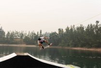 Mitte erwachsener Mann beim Wakeboarden von einer Rampe im Flusswasser — Stockfoto