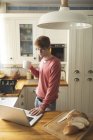 Людина, використовуючи ноутбук під час за кавою в кухні в домашніх умовах — стокове фото
