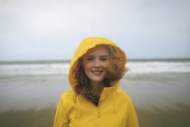 Portrait of redhead woman in yellow jacket standing in the beach. — Stock Photo