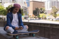 Усміхнена жінка скейтбордистка слухає музику на мобільному телефоні — стокове фото