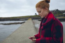 Рыжая женщина с мобильного телефона на пляже . — стоковое фото