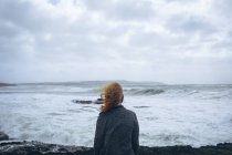 Rückansicht einer rothaarigen Frau, die am Strand mit Blick auf das Meer steht. — Stockfoto