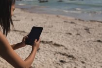 Женщина с цифровым планшетом на песчаном берегу моря — стоковое фото
