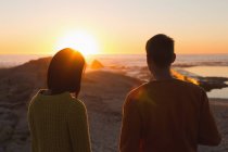 Visão traseira do casal em pé na praia durante o pôr do sol — Fotografia de Stock