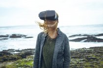 Mujer pelirroja usando auriculares de realidad virtual en la playa . - foto de stock