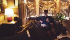 Пара використовує ноутбук у вітальні з казковими вогнями вдома — стокове фото