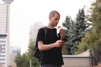 Молодий чоловік використовує мобільний телефон, маючи бургер — стокове фото