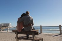 Visão traseira do casal sentado no banco perto da praia — Fotografia de Stock
