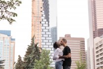 Romantic young couple kissing in city against buildings — Stock Photo