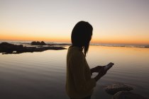 Frau benutzt Handy am Strand bei Sonnenuntergang — Stockfoto