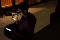 Executivo feminino tomando café enquanto usa tablet digital no escritório à noite — Fotografia de Stock
