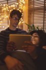 Pareja usando tableta digital en la sala de estar con luces de hadas en casa — Stock Photo