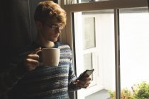 Чоловік використовує мобільний телефон, маючи каву вдома — стокове фото