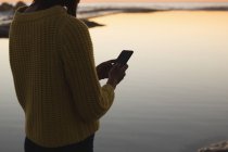 Середина жінки, використовуючи мобільний телефон на пляжі під час заходу сонця — стокове фото