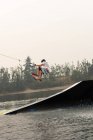 Mid adult man wakeboarding from ramp in river water — Stock Photo