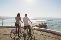 Coppia con biciclette in piedi sul lungomare vicino alla spiaggia — Foto stock