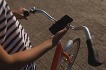 Partie médiane de la femme avec vélo en utilisant le téléphone mobile sur la promenade — Photo de stock