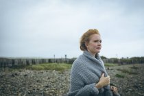 Thoughtful redhead woman in grey jacket standing near beach. — Stock Photo