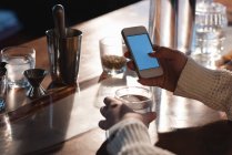 Крупный план женских рук с помощью мобильного телефона за барным столом — стоковое фото