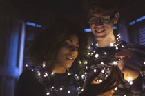 Happy couple playing with fairy lights at home — Stock Photo