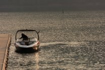 Homme méconnaissable debout sur un bateau à moteur dans la rivière au crépuscule — Photo de stock