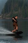 Jovem salpicando água enquanto wakeboarding no rio — Fotografia de Stock