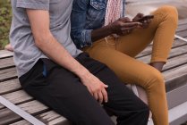 Mid section of couple sitting on bench and using mobile phone — Stock Photo