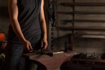 Mid section of female metalsmith holding tool in factory — Stock Photo