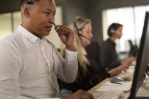 Executivos de atendimento ao cliente conversando no fone de ouvido na mesa no escritório — Fotografia de Stock