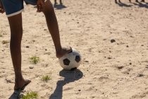 Низкая часть мальчика играет в футбол в земле — стоковое фото